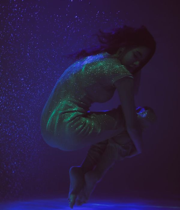Woman in a calm yoga pose in a dark room with light blue highlights.